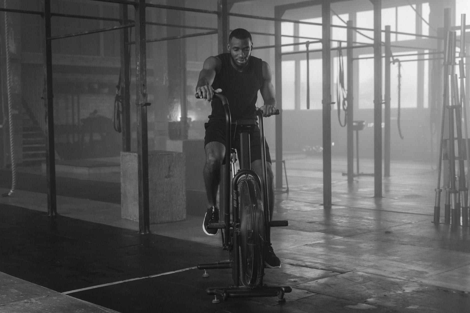 a grayscale of a man training on an air bike